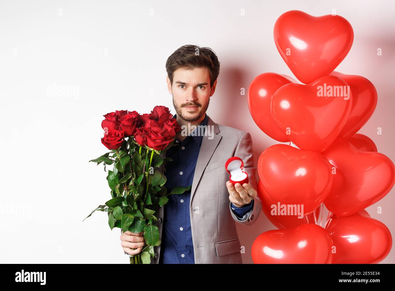 Romance de san valentín. hombre joven con ramo de rosas rojas y globos de  corazón sonriendo, trae regalos para el amante en la fecha de san valentín,  de pie sobre fondo azul.