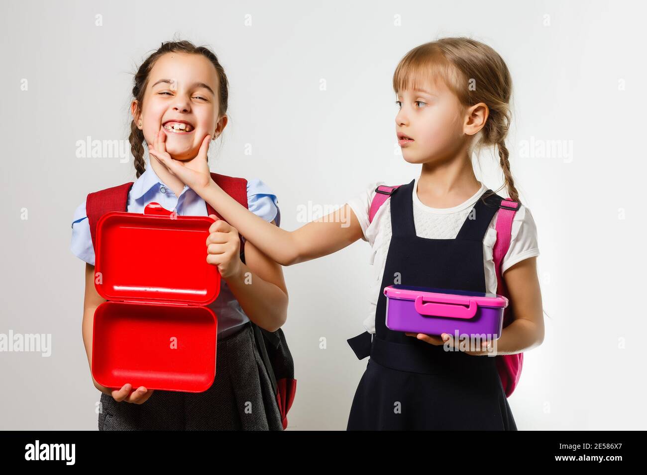 Alumnos de la escuela primaria con fiambreras en las manos. Las niñas con mochilas están comiendo fruta. Comienzo de las lecciones. Primer día de otoño. Foto de stock