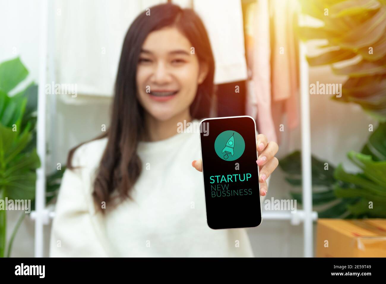 Joven feliz confidente dueño de la pequeña empresa mujer asiática mostrando smartphone con pantalla para el nuevo negocio de inicio con icono de lanzamiento de cohete. Foto de stock