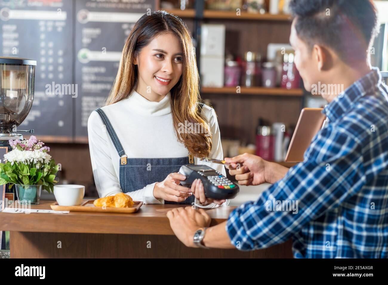Un cliente asiático que paga con tarjeta de crédito a través de la tecnología nfs sin contacto a un barista asiático del dueño de una pequeña empresa en la mesa de la cafetería, pequeña Foto de stock