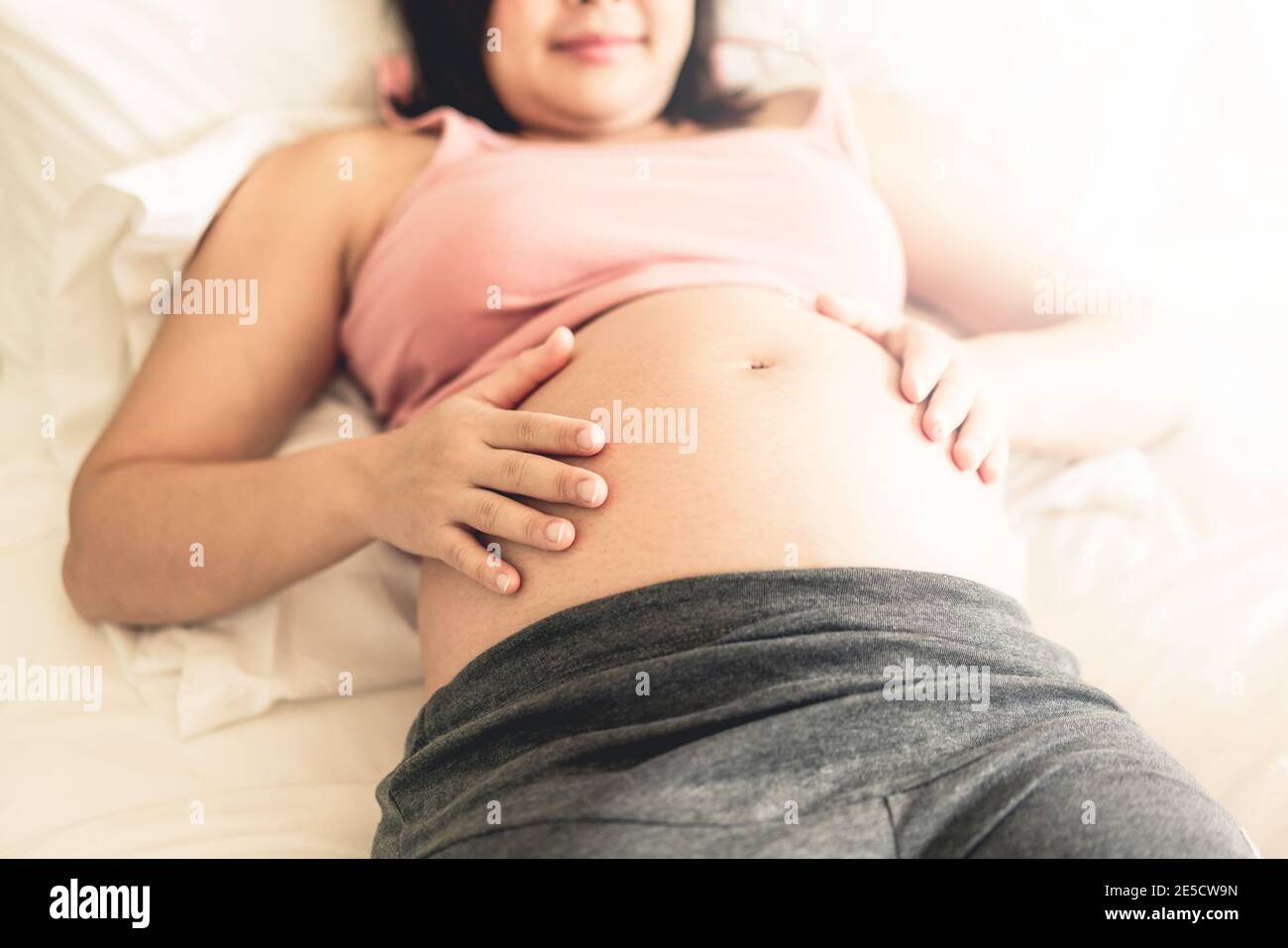 Mujer embarazada que se siente feliz en casa mientras cuida de su hijo. La joven que espera que la madre tenga a su bebé en el vientre embarazada. Maternidad prenatal Foto de stock