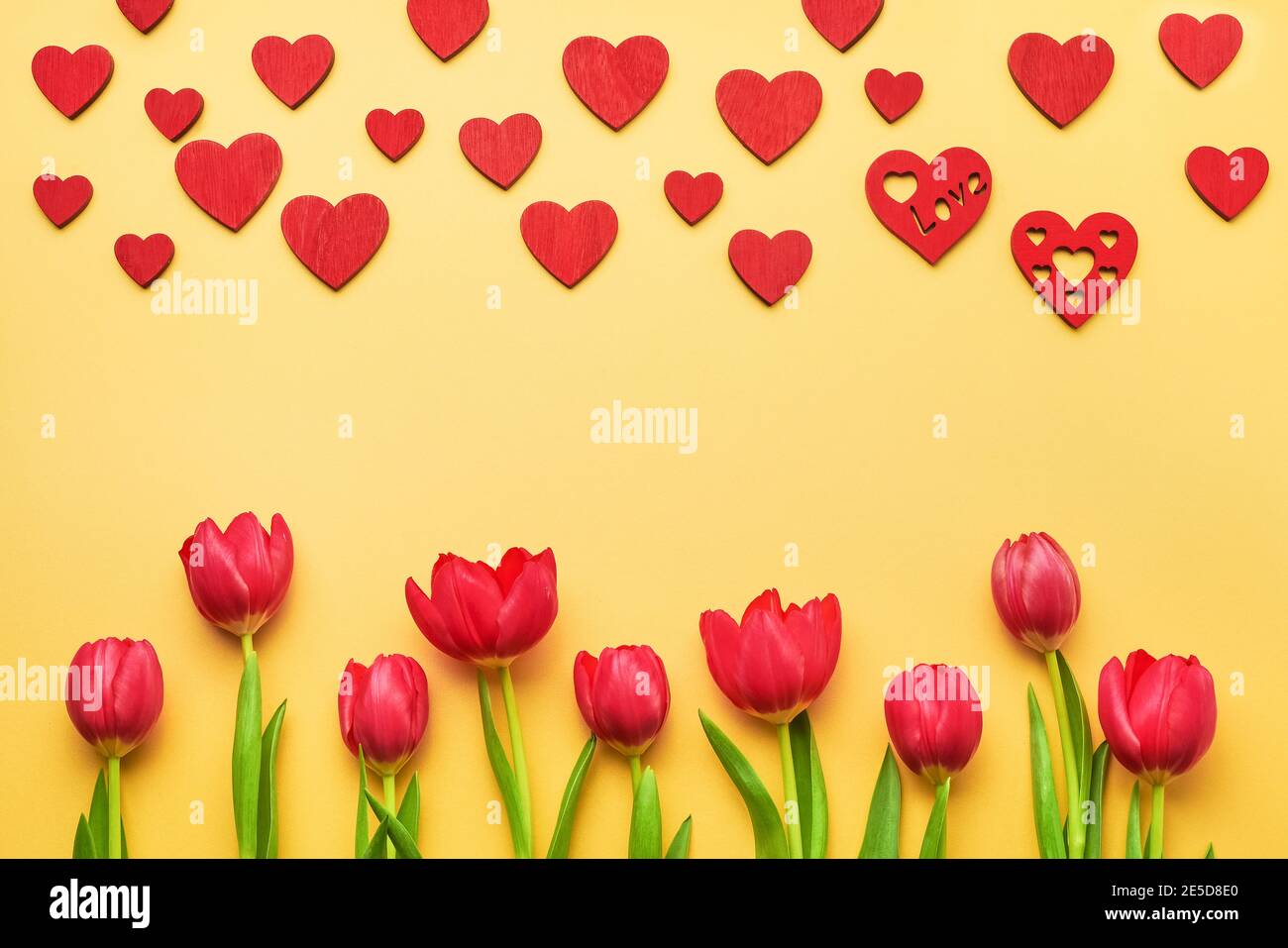 Tarjeta de felicitación para San Valentín. Ramo de tulipanes rojos y corazones rojos sobre fondo amarillo Foto de stock