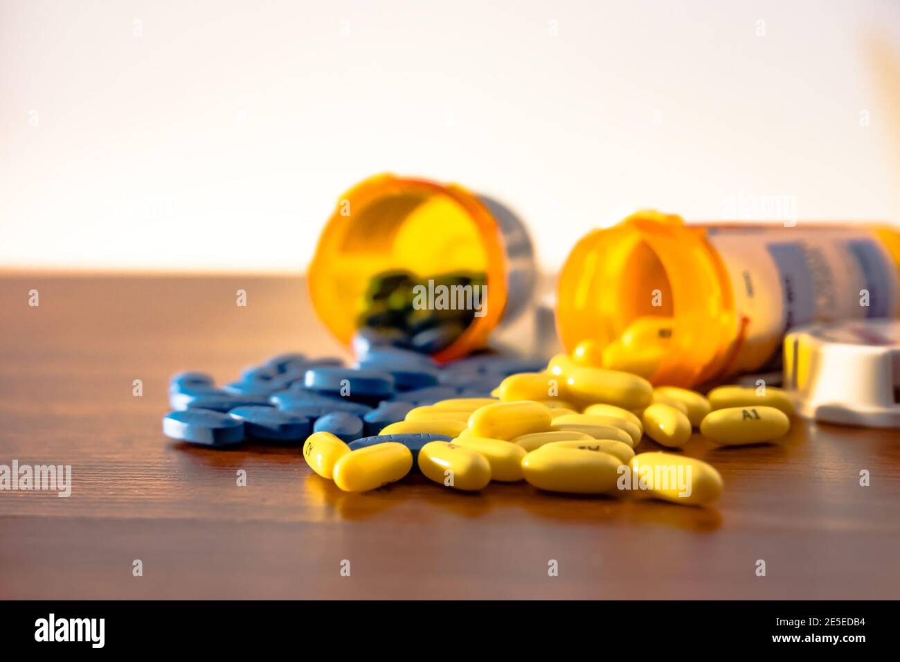 Dos botellas de prescripción revocadas con píldoras azules y amarillos derramando sobre la mesa de madera con fondo de Pentecostés. Foto de stock