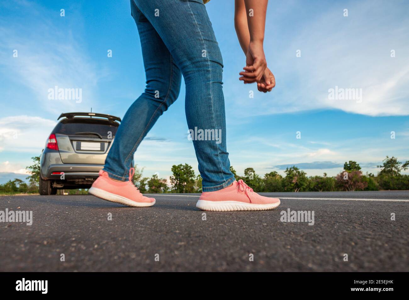 Mujeres con jeans que atan zapatillas en la carretera, coche estacionado  durante el día, el cielo azul brillante y las nubes de fondo Fotografía de  stock - Alamy