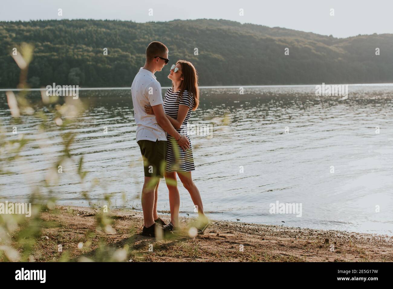 Retrato de pareja enamorada en la playa al atardecer. Toda la duración de la joven y el hombre abrazando al lago en la cálida noche de verano. Foto de stock