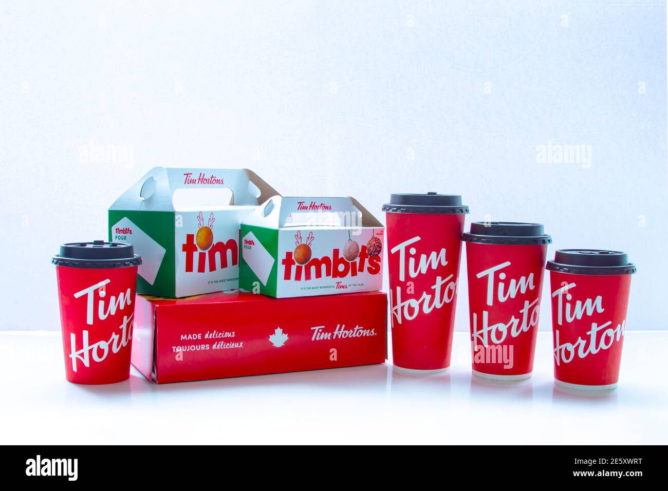 Calgary, Alberta. Canadá. 28 de enero de 2021. Varias tazas de café Tim Hortons de diferentes tamaños con cajas de timbits y donuts sobre fondo blanco. Foto de stock