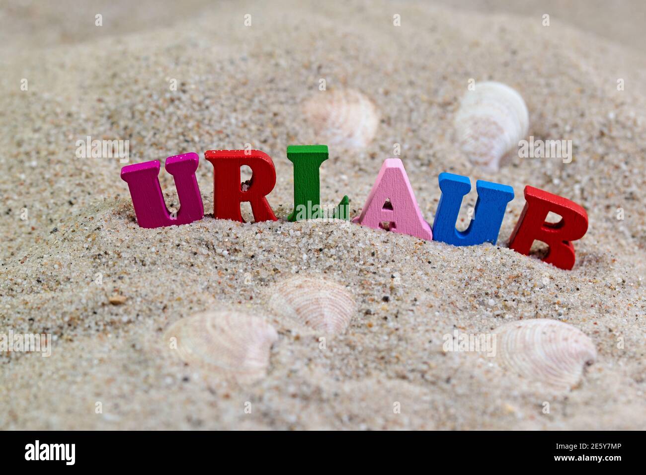 Letras de madera de colores en la arena con el texto 'Urlaub', traducción 'vacaciones' Foto de stock