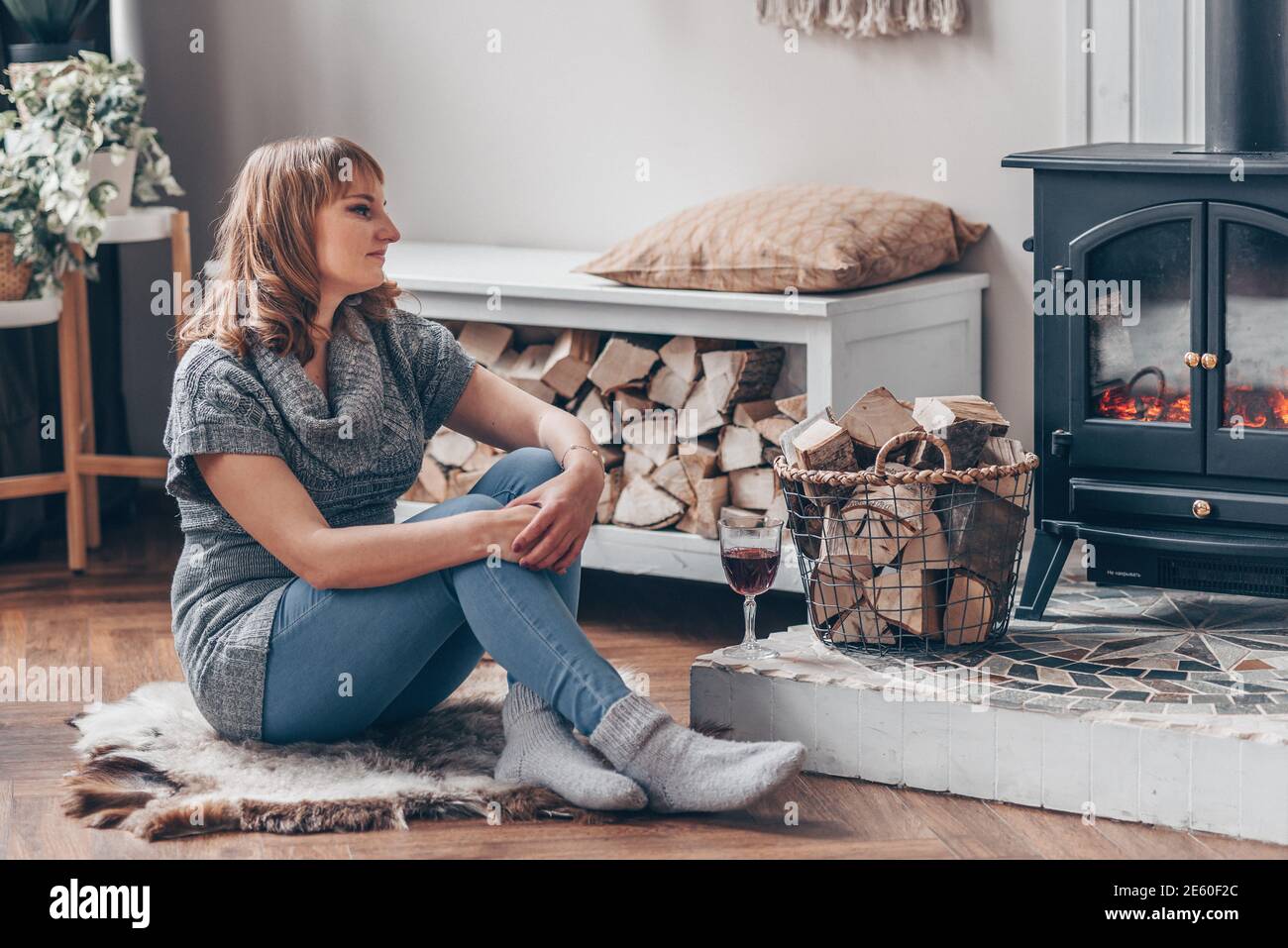 Mujer joven y sonriente se sienta cerca de la fogata en otoño o, casa en el bosque. Concepto de relajación invernal. Foto de stock