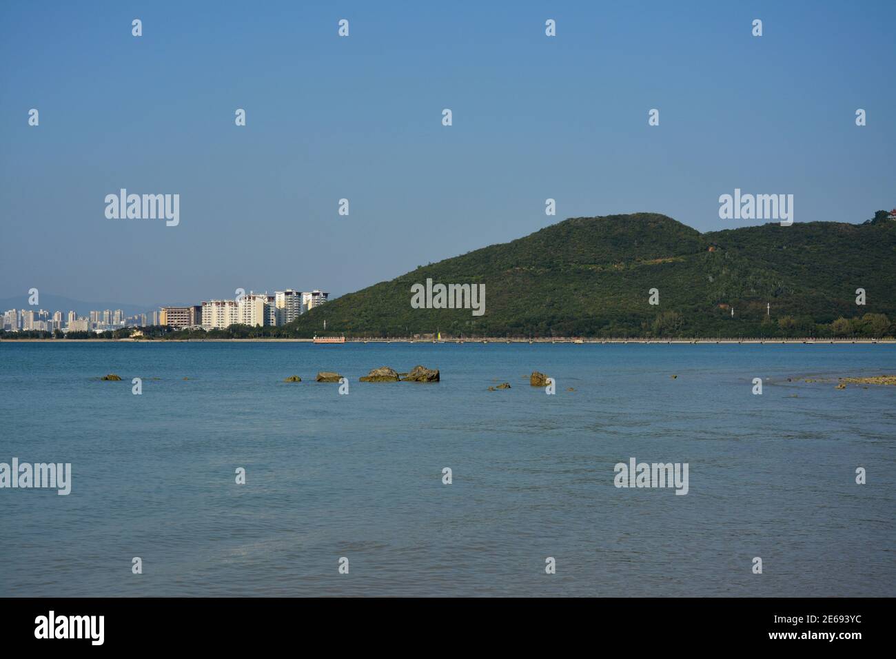 vista azul al mar con montañas y edificios bajo el cielo despejado en el día soleado Foto de stock