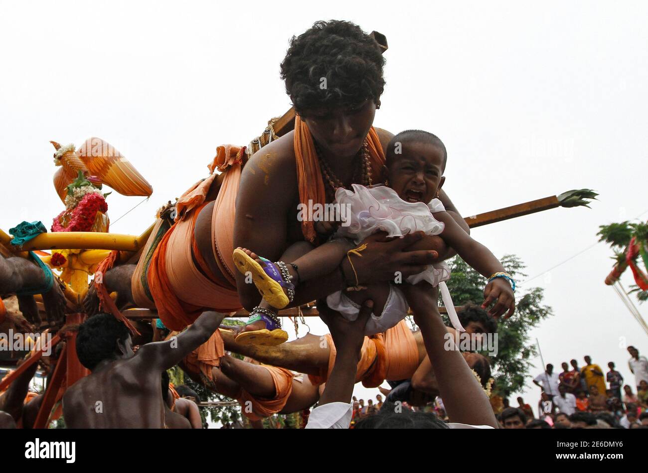 Hindu devotees carry their children as they hang from wooden poles