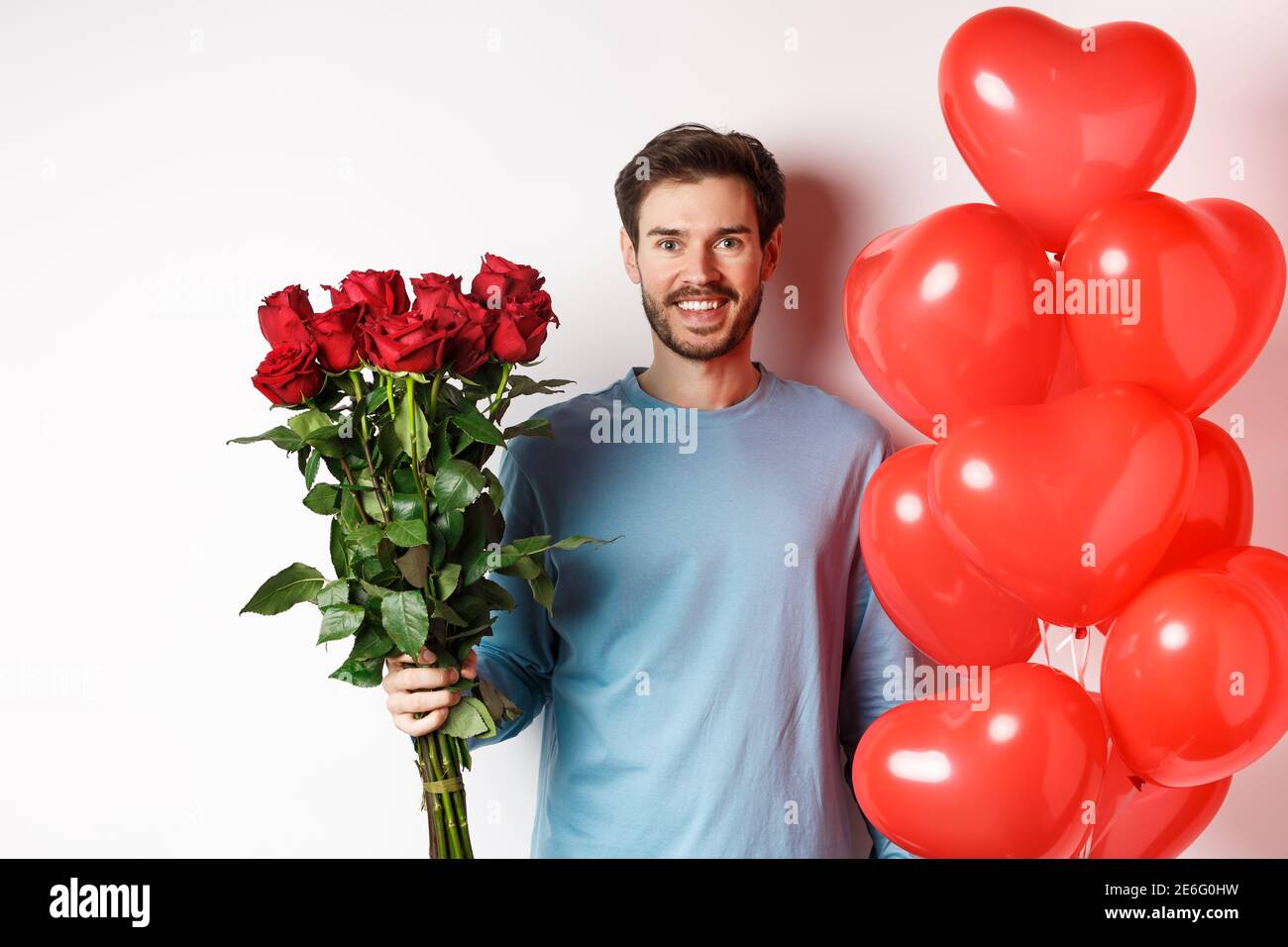 Romance de san valentín. hombre joven con ramo de rosas rojas y globos de  corazón sonriendo, trae regalos para el amante en la fecha de san valentín,  de pie sobre fondo azul.