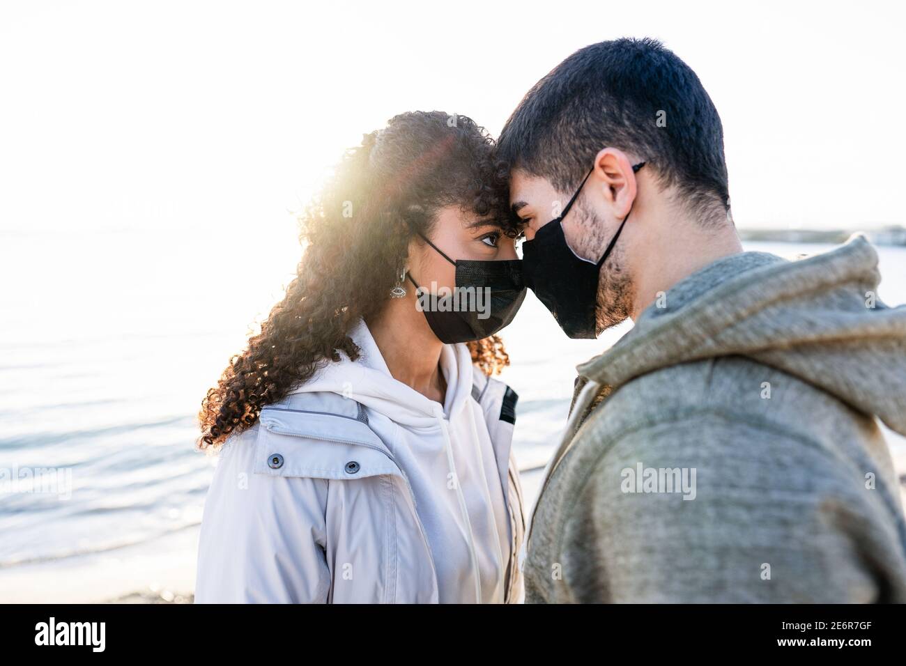 Nueva pareja normal en problemas de amor debido a distanciamiento social: Hombre y novia mirando en los ojos uno a otro cabeza con el sol de puesta refl Foto de stock