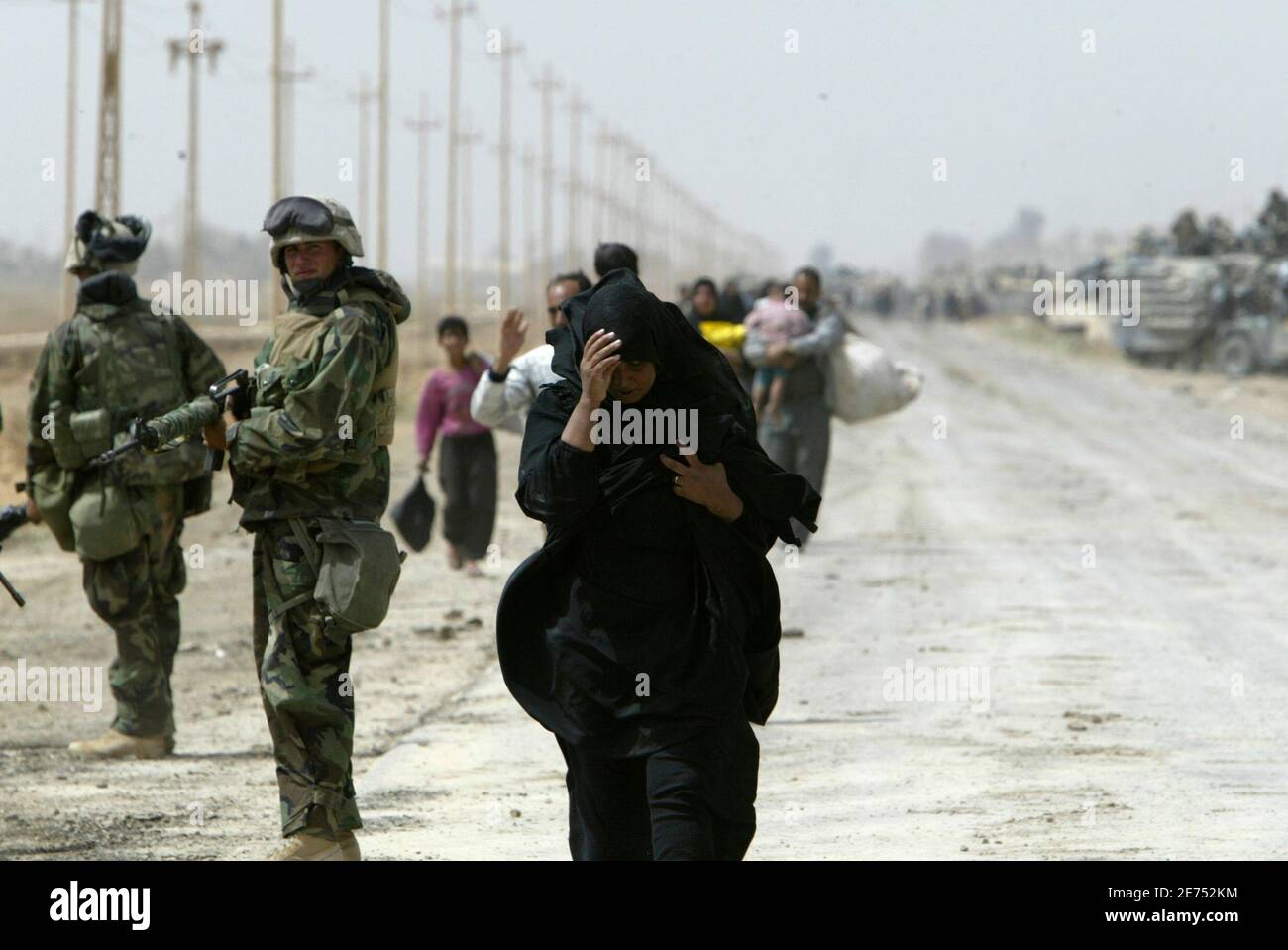 An Iraqi woman, a refugee from Baghdad, walks next to a U.S. Marine from Lima Company, a part of the 7th Marine Regiment, on the road south-east of the Iraqi capital April 5, 2003. U.S. Marine commander said on Saturday American troops would use overwhelming force to crush any resistance if ordered to storm Baghdad and that the battle would cost many civilian lives.   REUTERS/Oleg Popov   (IRAQ) Foto de stock