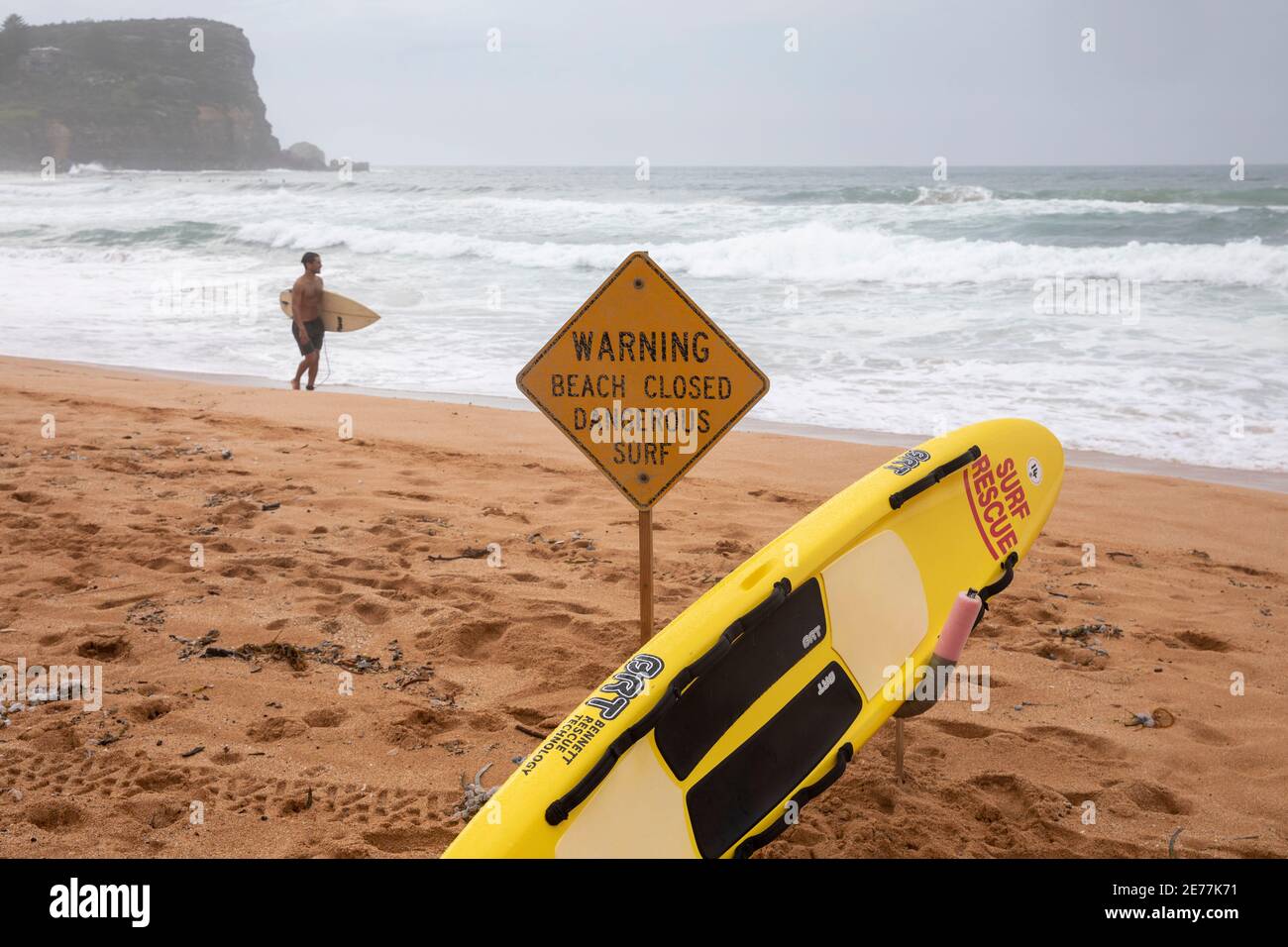 Advertencia: La playa está cerrada. Hay un cartel de surf peligroso cuando los surfistas caminan por Avalon Beach, Sydney, Australia Foto de stock