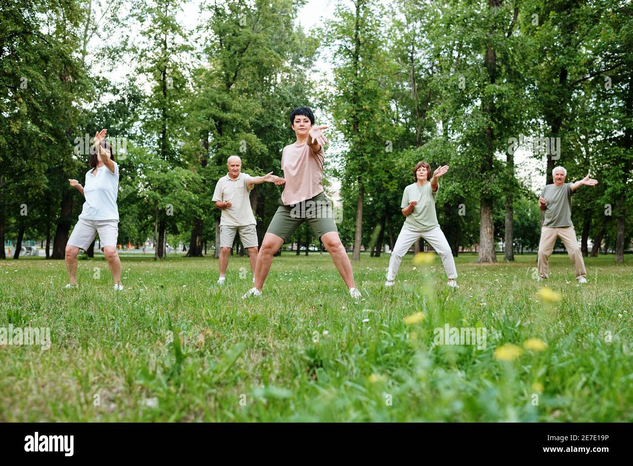 Mujer madura mostrando los ejercicios a la gente mientras ellos de pie en la hierba al aire libre Foto de stock