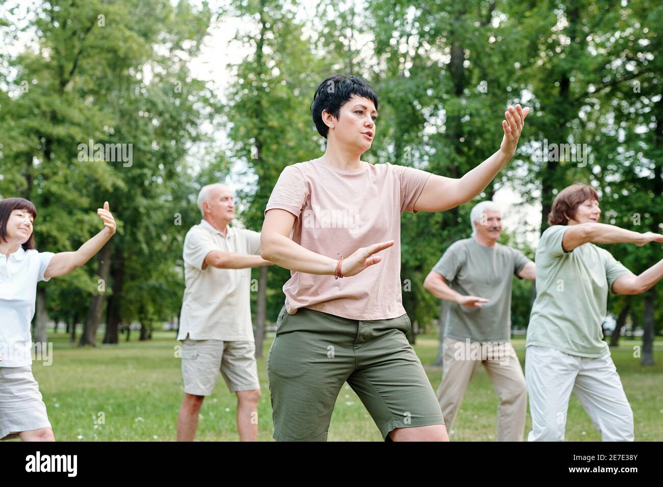 Grupo de personas maduras haciendo ejercicios con entrenador en el estacione al aire libre Foto de stock