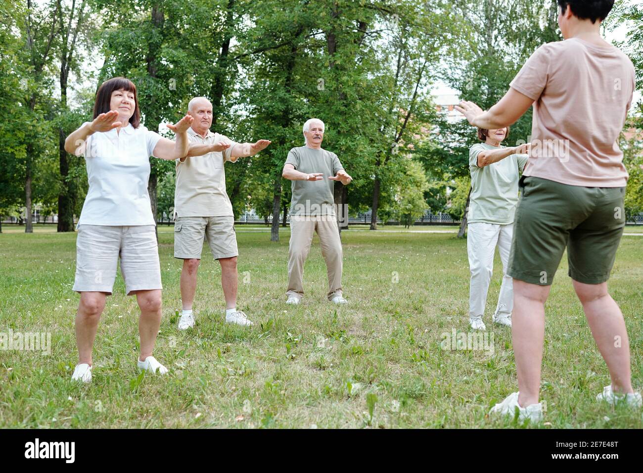 Mujeres y hombres maduros haciendo ejercicios junto con el entrenador el parque Foto de stock