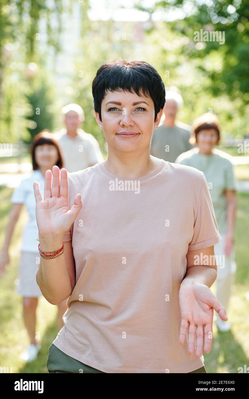 Retrato de una mujer madura sonriendo a cámara mientras hace ejercicios con sus manos en el parque al aire libre Foto de stock