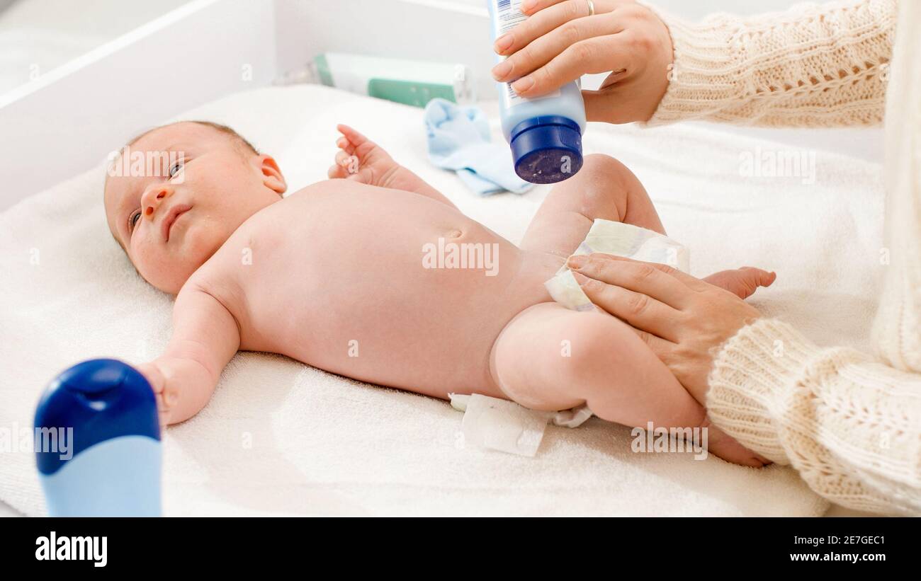 Bebé recién nacido acostado sobre mesa de cambio mientras la madre cambia  el pañal y aplica talco sobre la piel suave. Concepto de higiene de bebés y recién  nacidos y Fotografía de