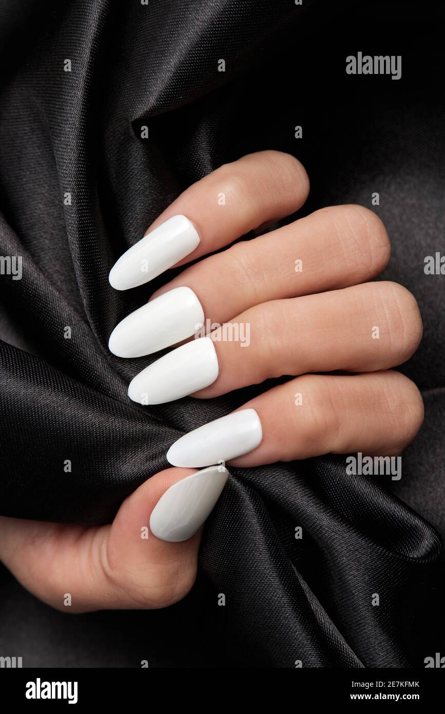 Mano femenina con uñas blancas largas que sostienen un satén negro tela  Fotografía de stock - Alamy