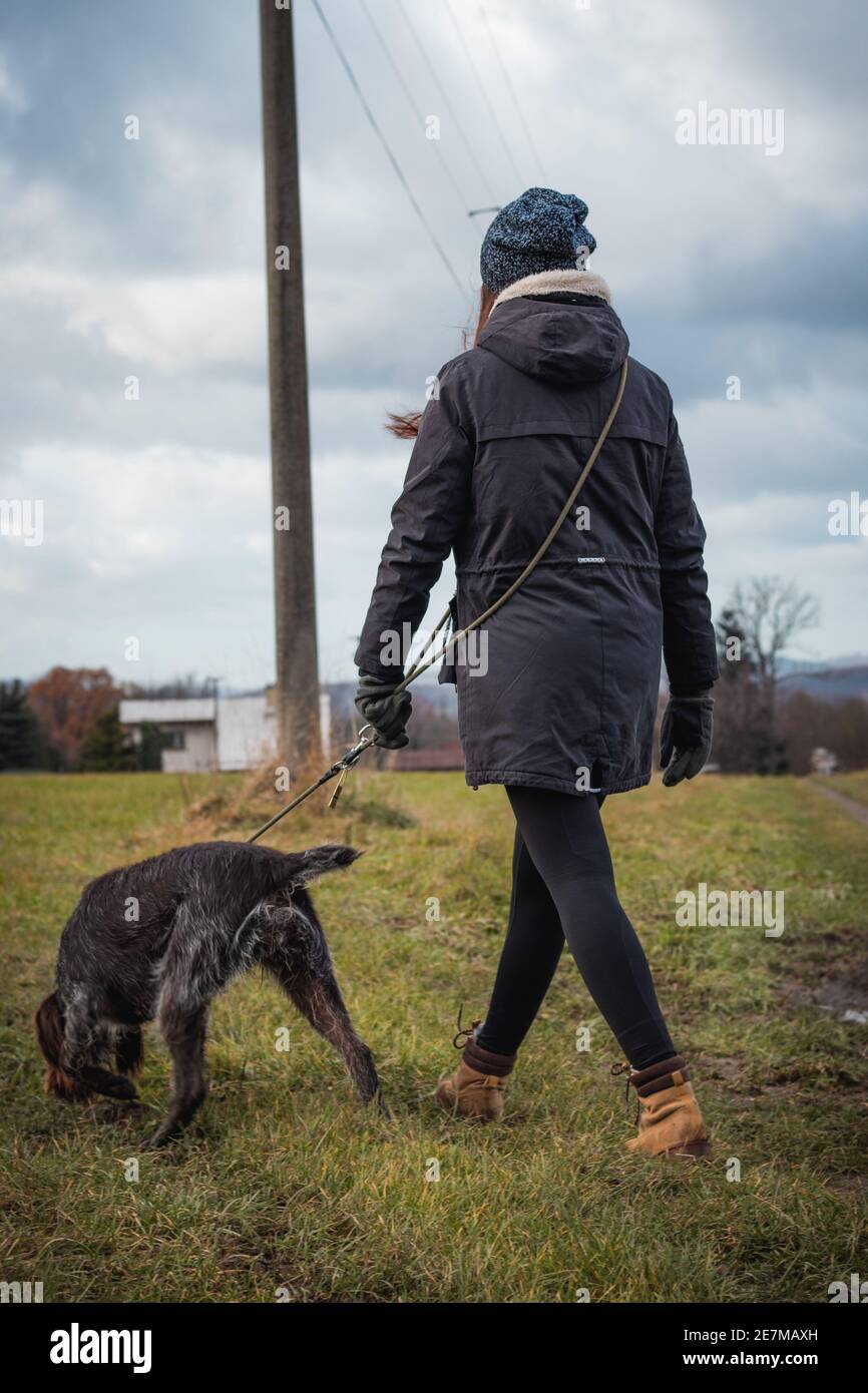 vínculo entre perro y mujer desde el nacimiento. Retrato franco de una  mujer con ropa de invierno y perro checo de pelo Bohemio apuntando Griffon  sobre un wildernes Fotografía de stock -