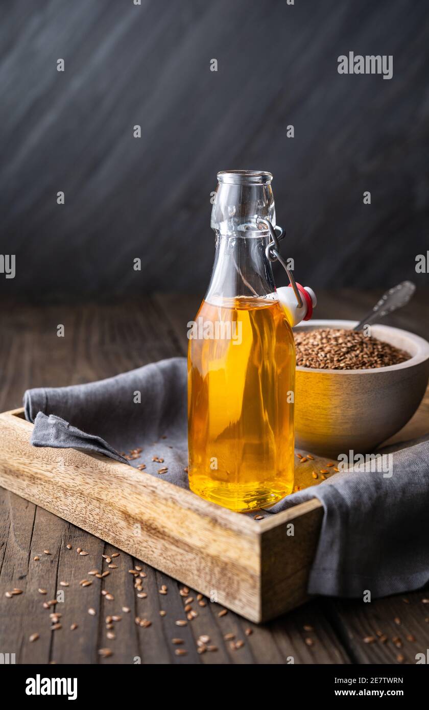 Aceite de linaza en botella de vidrio, decorado con semillas enteras sobre fondo de madera rústica con espacio de copia Foto de stock