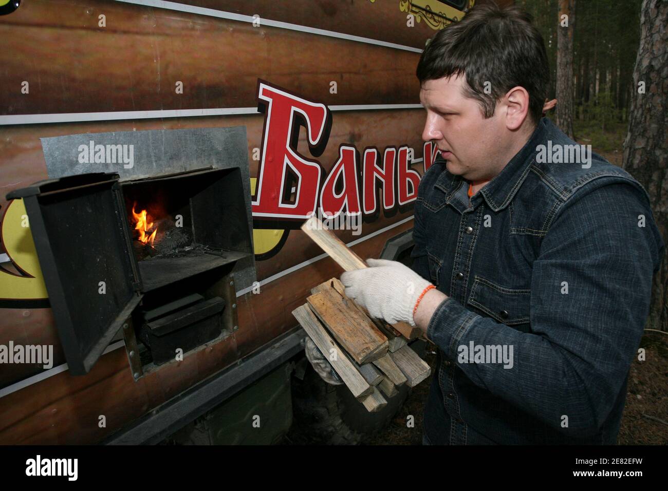 Un hombre alimenta el horno de una sauna móvil que se monta en un camión de tracción a las cuatro ruedas en un bosque en Barnaul, en la región de Altai 5 de abril de 2008. Un artesano local instaló la sauna rusa, o banya, en la cabina de un portador de personal de tracción en las cuatro ruedas y dijo que el robusto vehículo del ejército puede dominar casi cualquier terreno. REUTERS/Andrei Kasprishin (RUSIA) Foto de stock