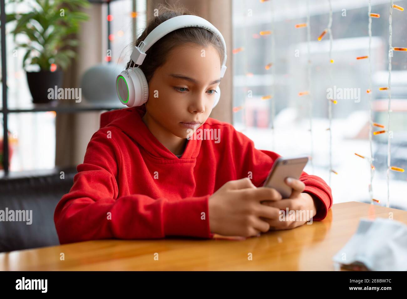 Foto de una adolescente en unos auriculares blancos durante las conversaciones en línea con amigos. Concepto de tecnología moderna. Foto de stock