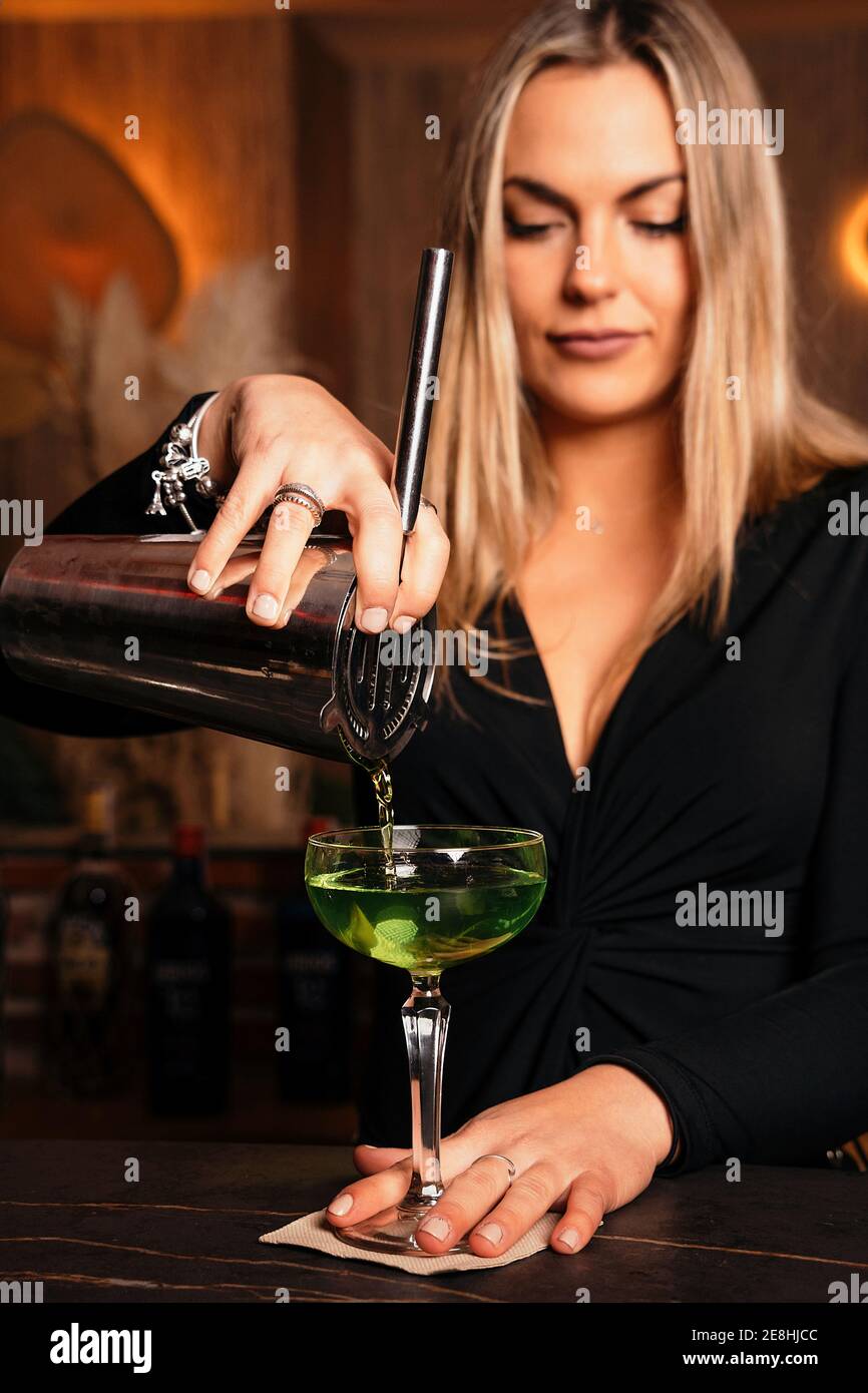 Hermosa mujer rubia joven barman en conjunto con estilo vertiendo alcohol  coctel de coctelera en elegante margarita en el restaurante Fotografía de  stock - Alamy