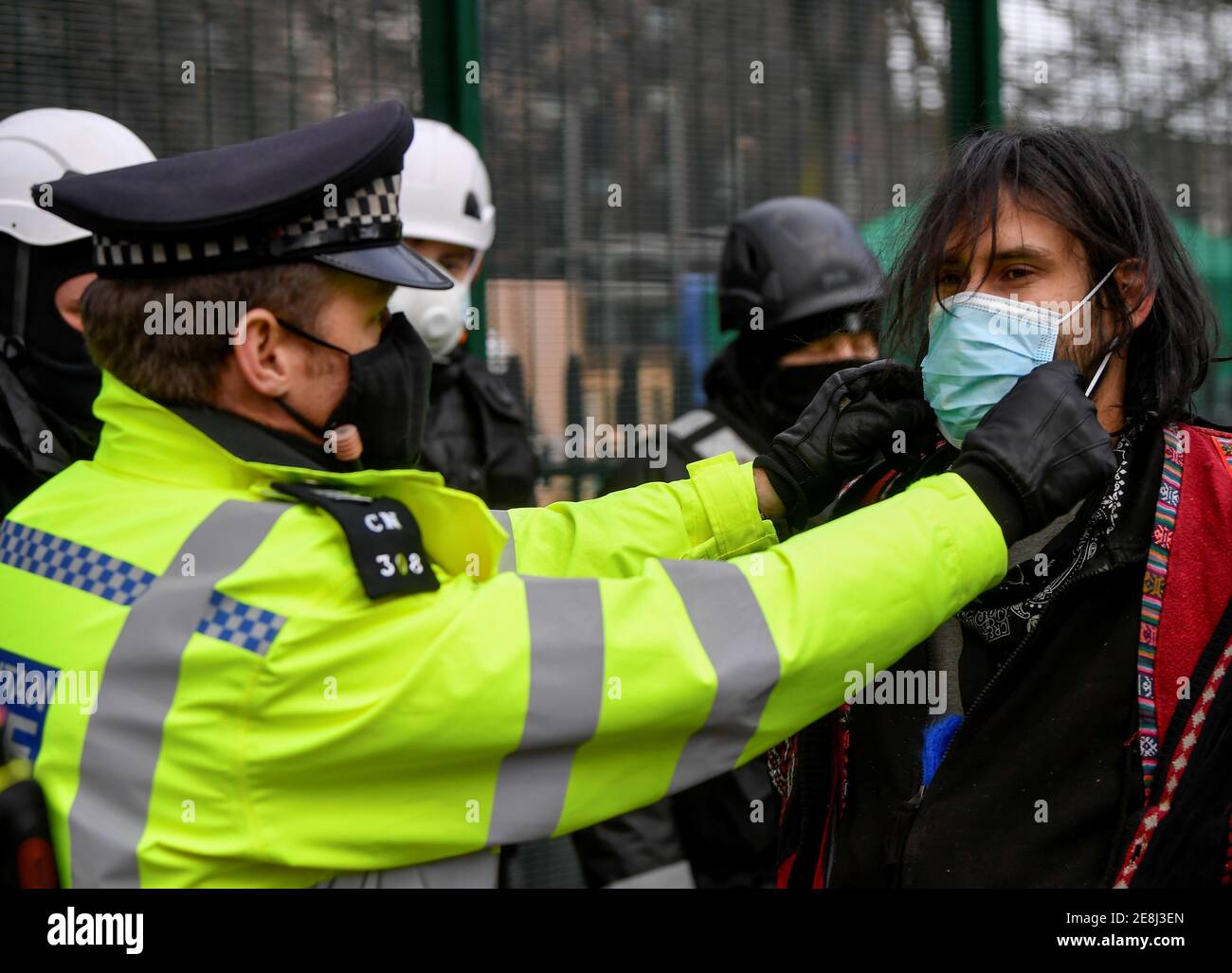 Un oficial de policía ajusta una máscara protectora a un manifestante mientras está detenido, ya que otros manifestantes ocupan túneles bajo Euston Square Gardens para protestar contra el ferrocarril de alta velocidad HS2 en Londres, Gran Bretaña, el 31 de enero de 2021. REUTERS/Toby Melville Foto de stock