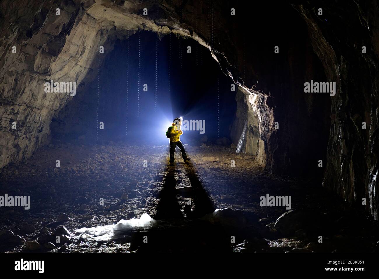 Niño de 11 años de edad de pie dentro de una cueva, iluminado por una luz de fondo, estalagmitas fundidas hechas de hielo en el frente, Eslovenia Foto de stock