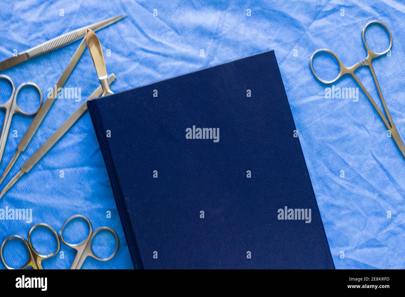 Una inyección de ángulo alto de un kit de disección cerca de a. libro azul sobre la mesa estéril Foto de stock