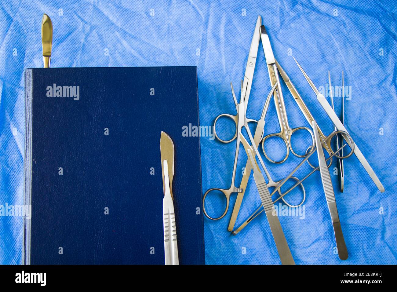 Una inyección de ángulo alto de un kit de disección cerca de a. libro azul sobre la mesa estéril Foto de stock