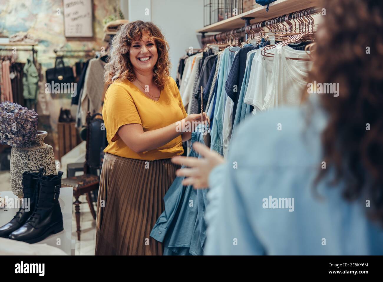 La vendedora femenina ayuda al comprador a elegir entre vestidos para comprar en la tienda de moda. Propietario de la tienda de ropa que ayuda al cliente en su tienda. Foto de stock