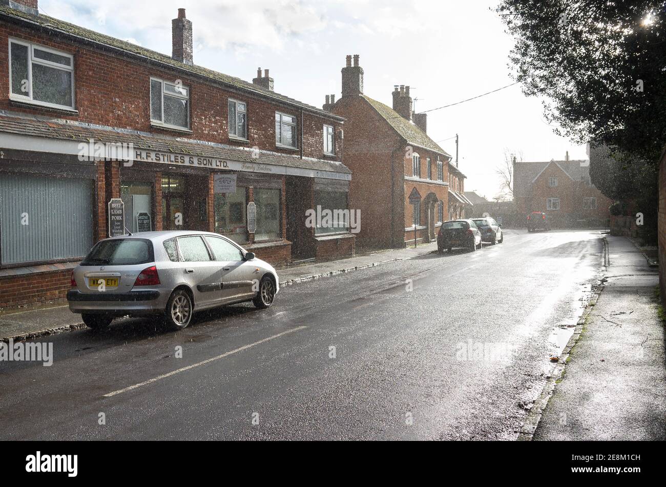 Una fuerte ducha de lluvia limpia la calle del pueblo en Bromham Cerca de Chippenham Wiltshire, Inglaterra, Reino Unido Foto de stock