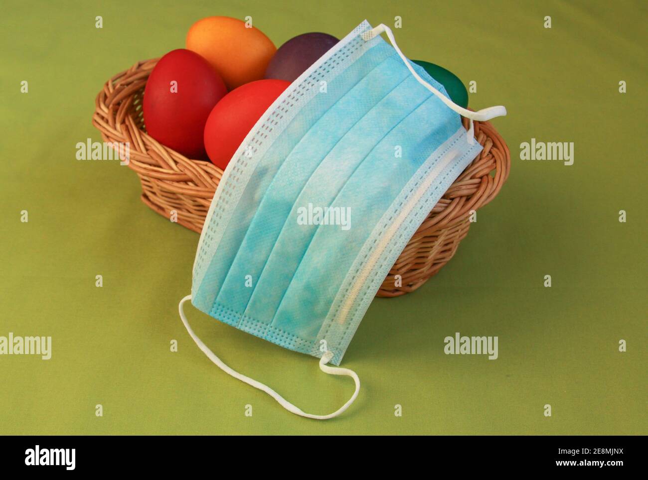 Huevos de Pascua pintados de color aislados en la decoración de la cesta de madera con máscara quirúrgica, un símbolo de la pandemia del coronavirus. Semana Santa 2020 covid 19 brote c Foto de stock