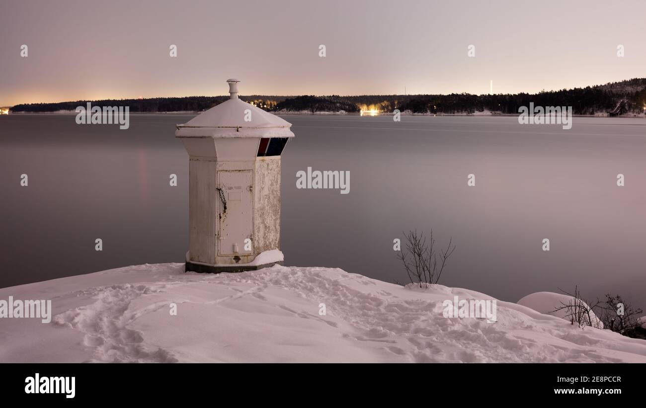 Faro blanco en la costa de Bogesundslandet hacia Lidingö, Suecia, cerca de Estocolmo, durante una noche de invierno Foto de stock