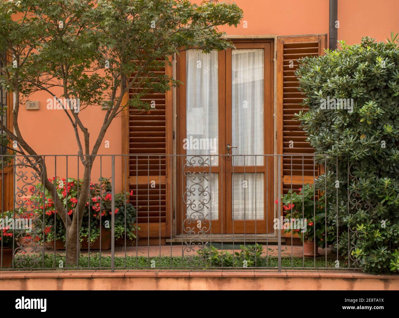 Este acogedor patio está en Lucca, Toscana, Italia. Persianas de madera, flores y verdor con cortinas transparentes son acogedoras. Foto de stock