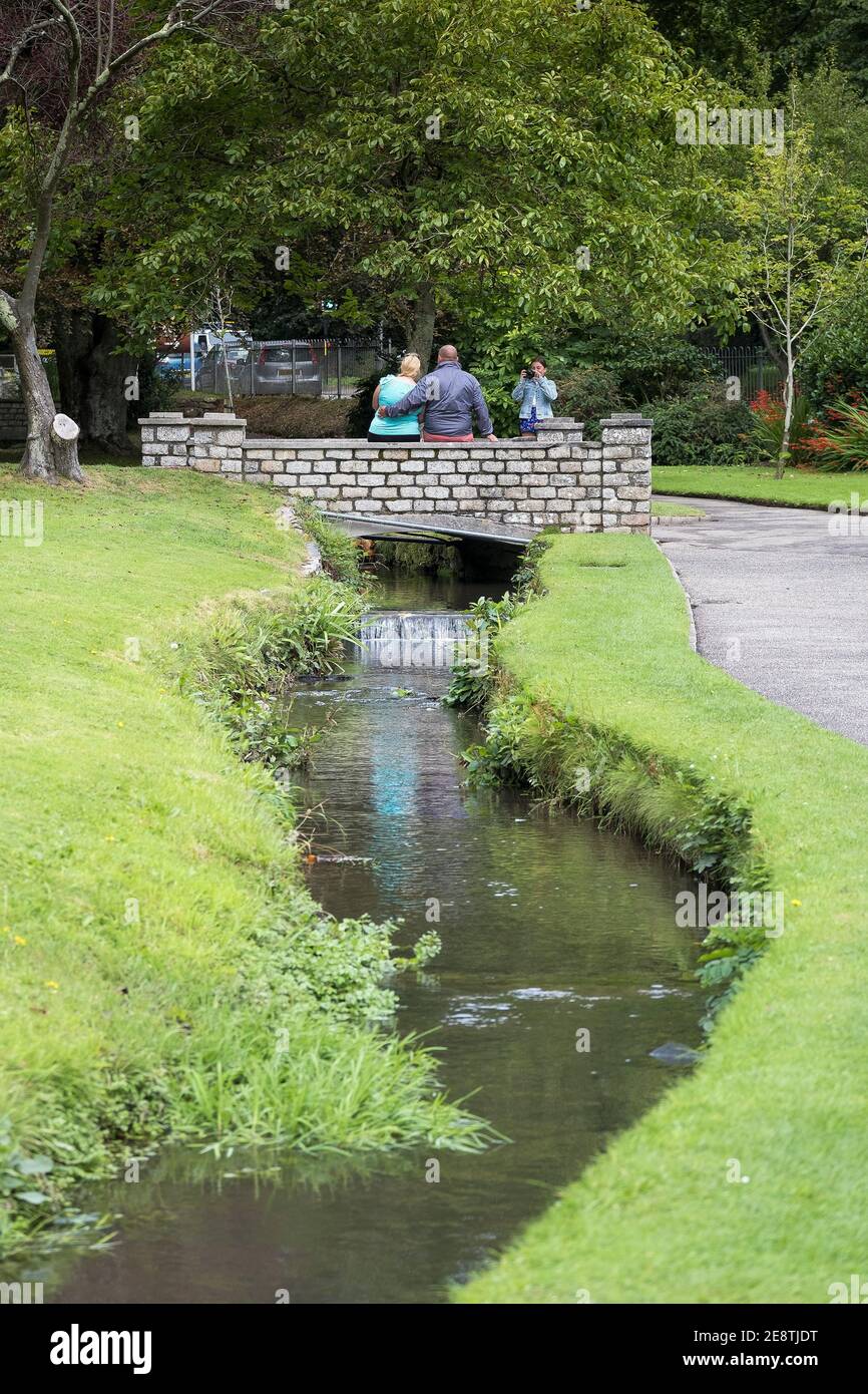 Turistas posando para una fotografía en un pequeño puente peatonal sobre un pequeño río en Trenance Gardens en Newquay en Cornwall. Foto de stock