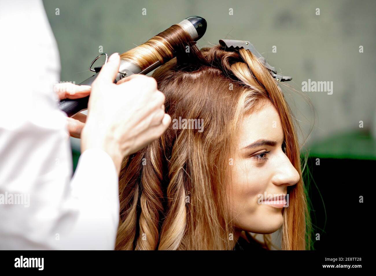 Peluquería profesional hace rizos con una plancha rizado para un mujer  joven con pelo largo rojo en un salón de belleza Fotografía de stock - Alamy