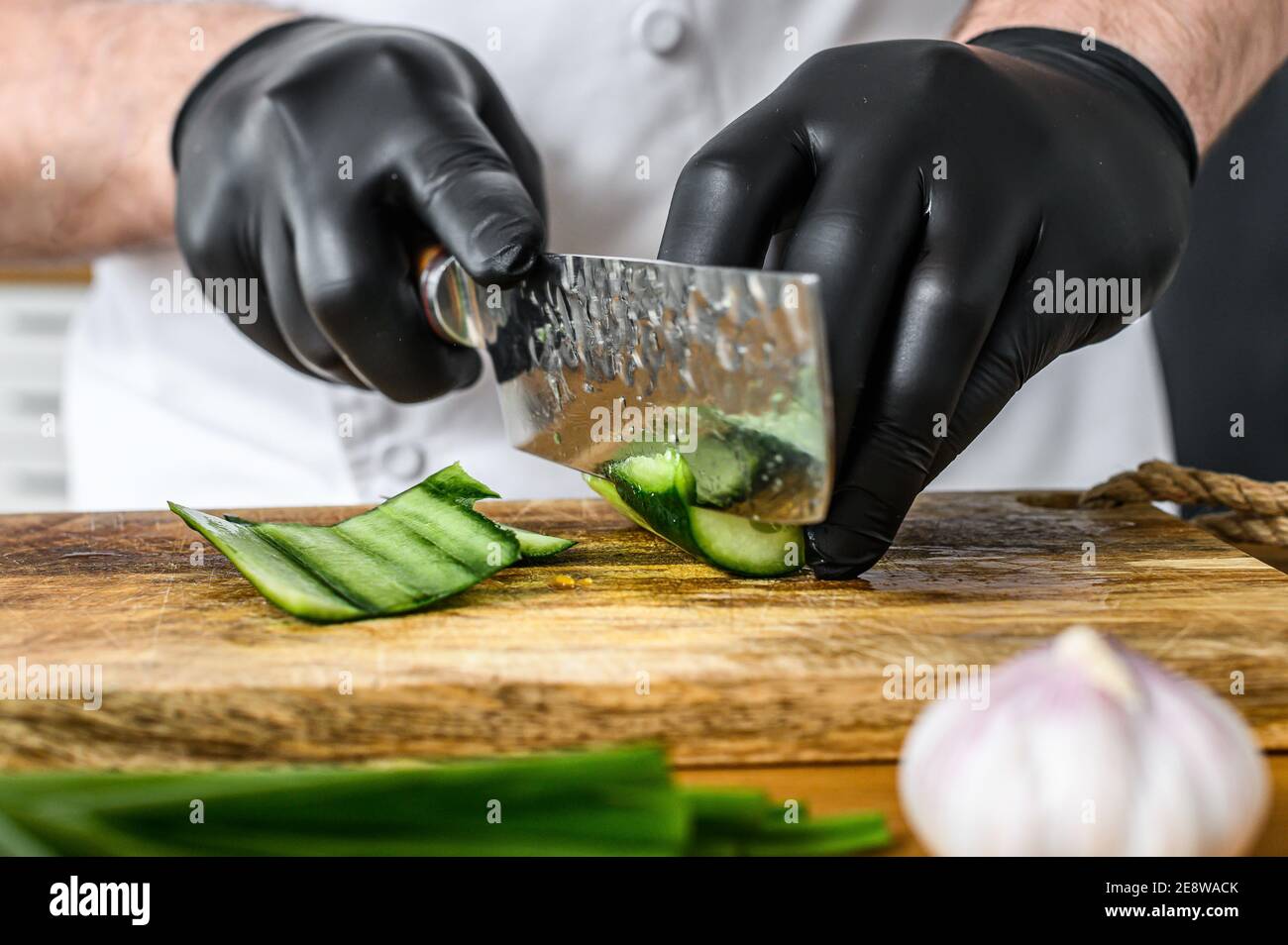 solamente social músculo Un chef en guantes negros está cortando un pepino verde fresco en una tabla  de cortar de madera. Concepto de cocinar alimentos orgánicos saludables  Fotografía de stock - Alamy
