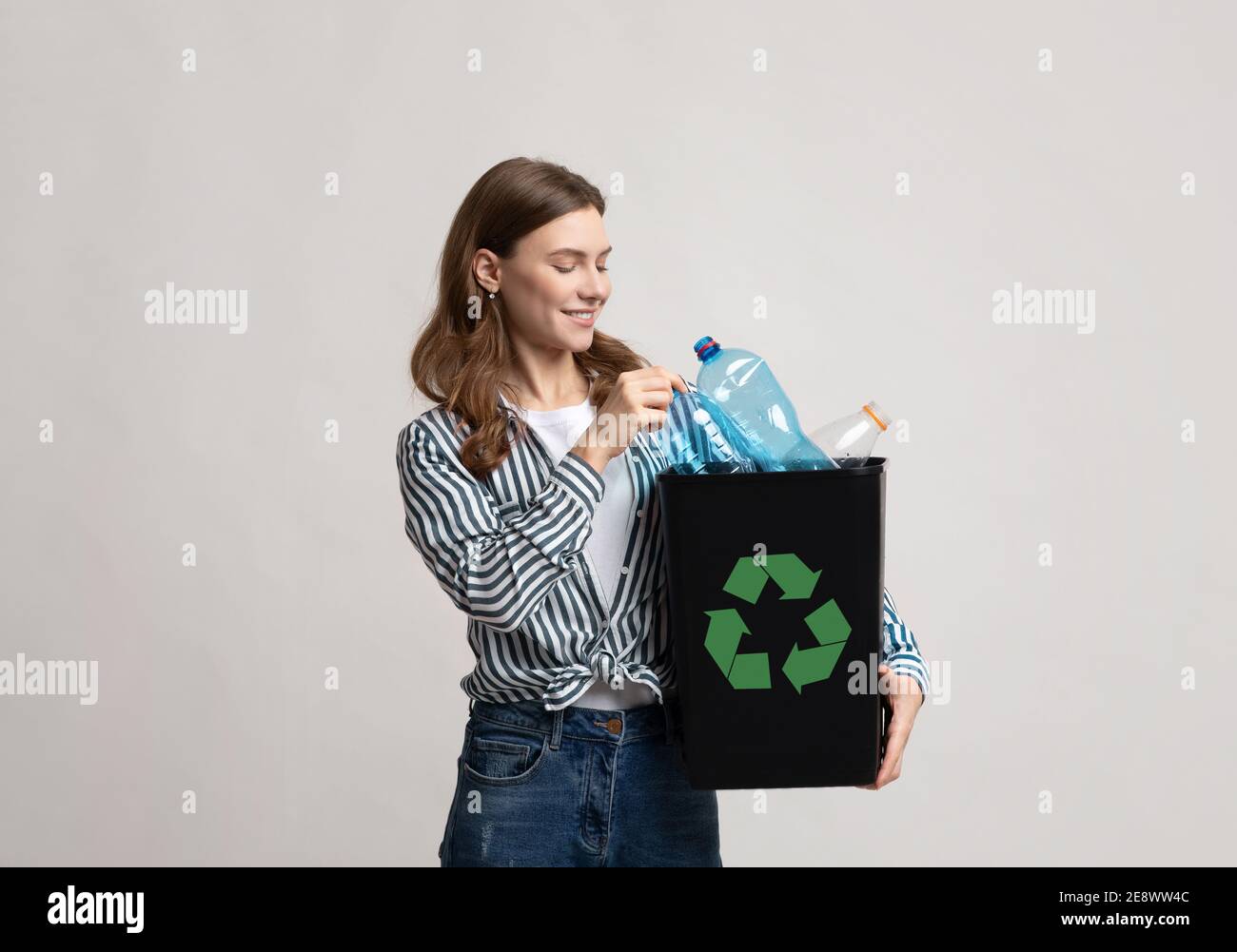 Reciclaje de residuos. Mujer joven sonriente sosteniendo un recipiente negro con botellas de plástico Foto de stock