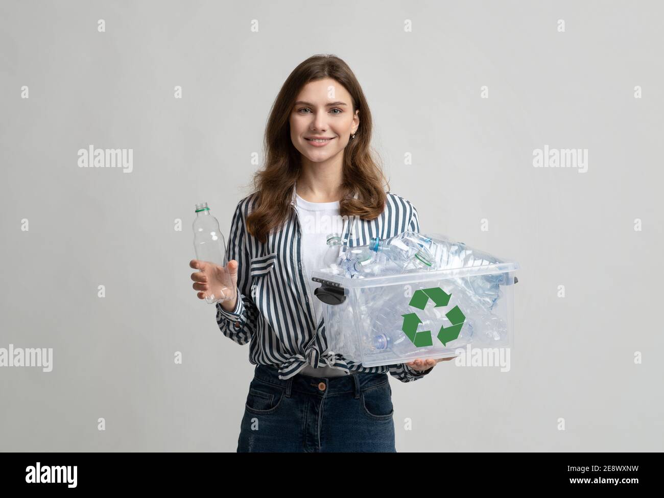 Reciclaje de plástico. Mujer joven sonriente recogiendo botellas para el reciclaje de residuos en el contenedor Foto de stock