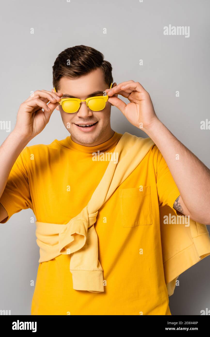 Hombre sonriente sosteniendo gafas de sol amarillas sobre fondo gris  Fotografía de stock - Alamy