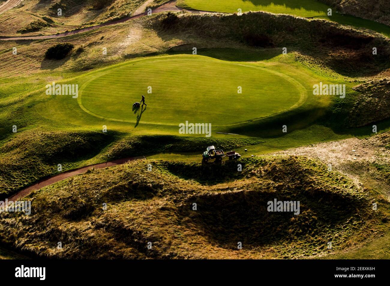 Un portero en el Wallasey Golf Club, Wirral mofa el verde durante el cierre de seguridad el 1 de febrero de 2021. Los clubes de golf de todo el Reino Unido siguen bajo estricto retri Foto de stock