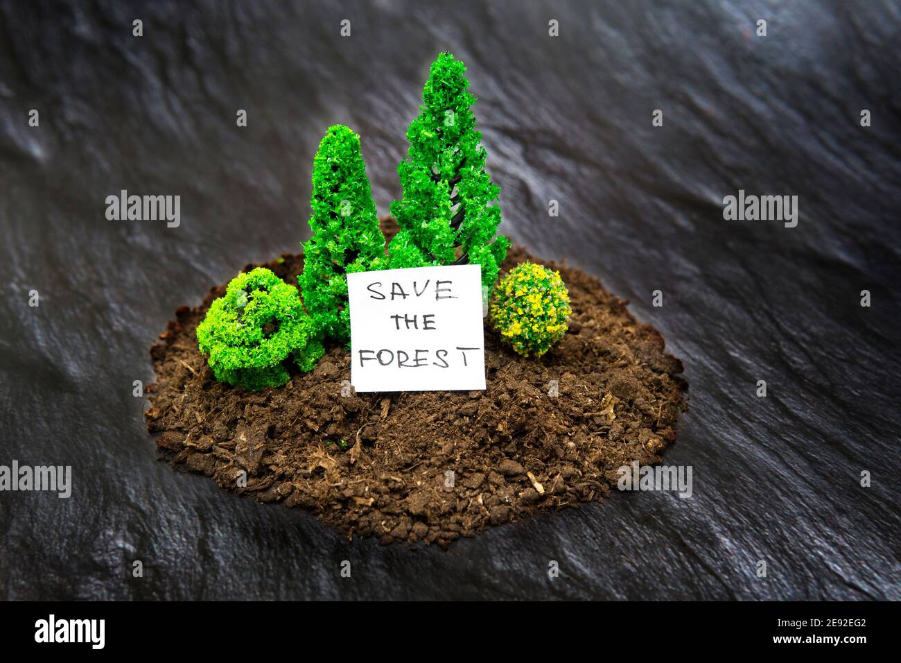 Composición de bosque de juguete en miniatura hecha de algunos árboles de suelo y de juguete sobre fondo de textura negra imitación tierra quemada. Concepto de parada de incendios forestales. Foto de stock