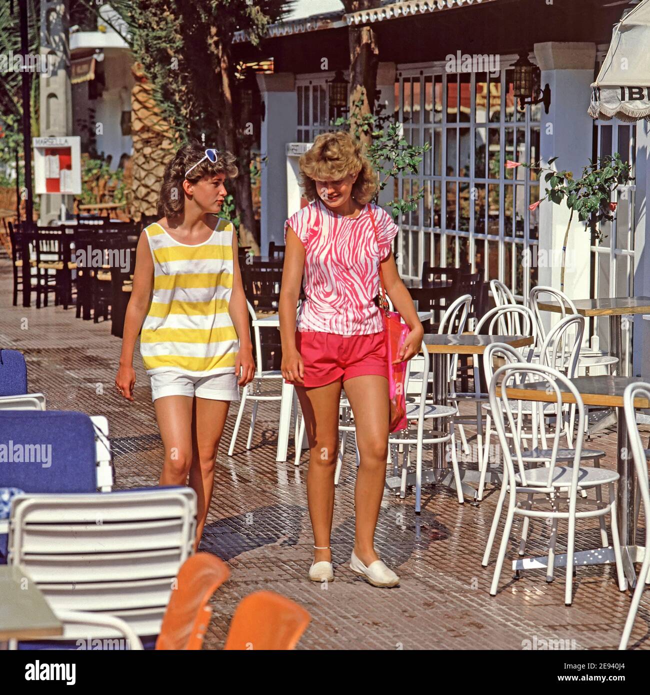 Dos niñas modelo de adolescentes la moda de los años 80 caminando al aire libre Pueblo costero español de Cala d'Or un paquete familiar Vacaciones en Mallorca España Fotografía de