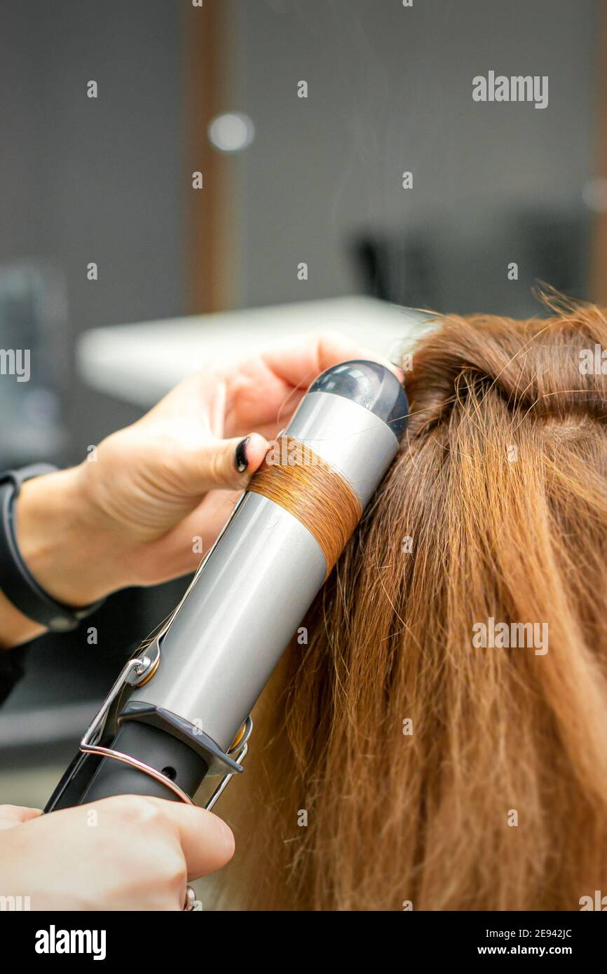 Peluquería profesional hace rizos con una plancha rizado para un mujer  joven con pelo largo rojo en un salón de belleza Fotografía de stock - Alamy