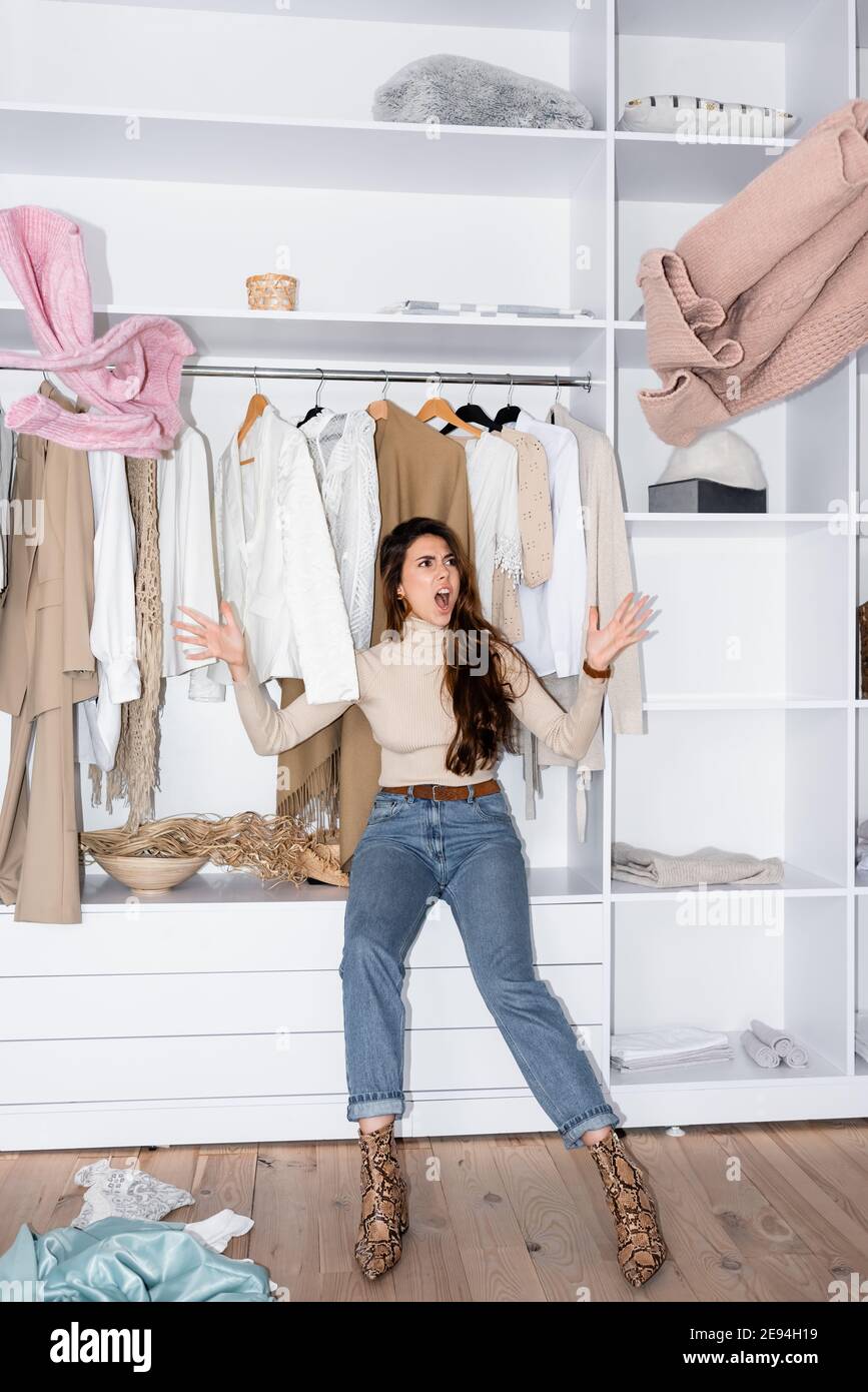 Mujer enojada tirando ropa mientras se sienta en el estante en el armario  Fotografía de stock - Alamy