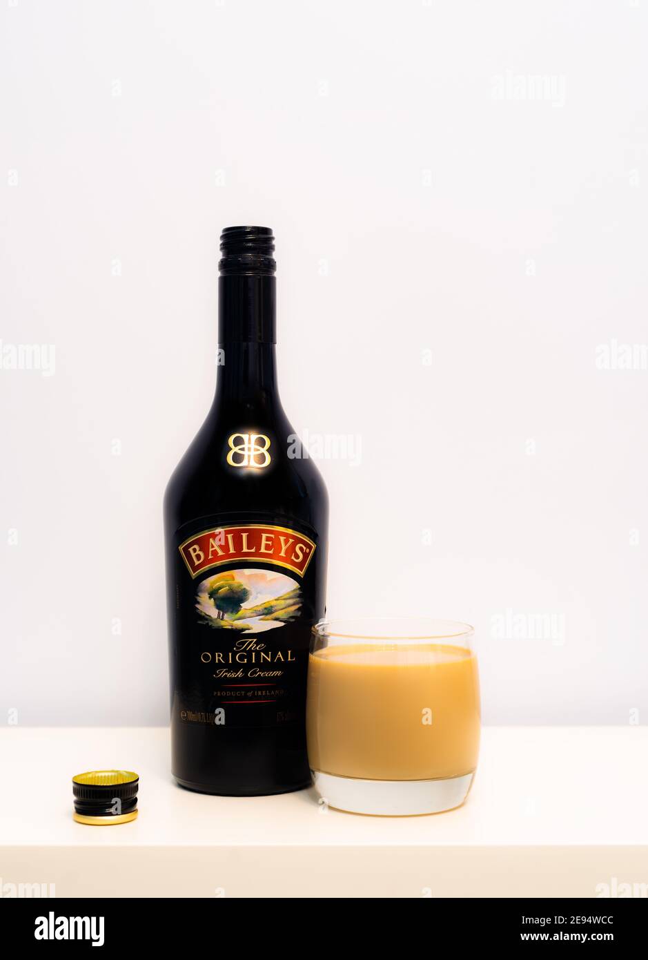 Botella abierta de licor Baileys con vidrio lleno de pie en el blanco Foto de stock